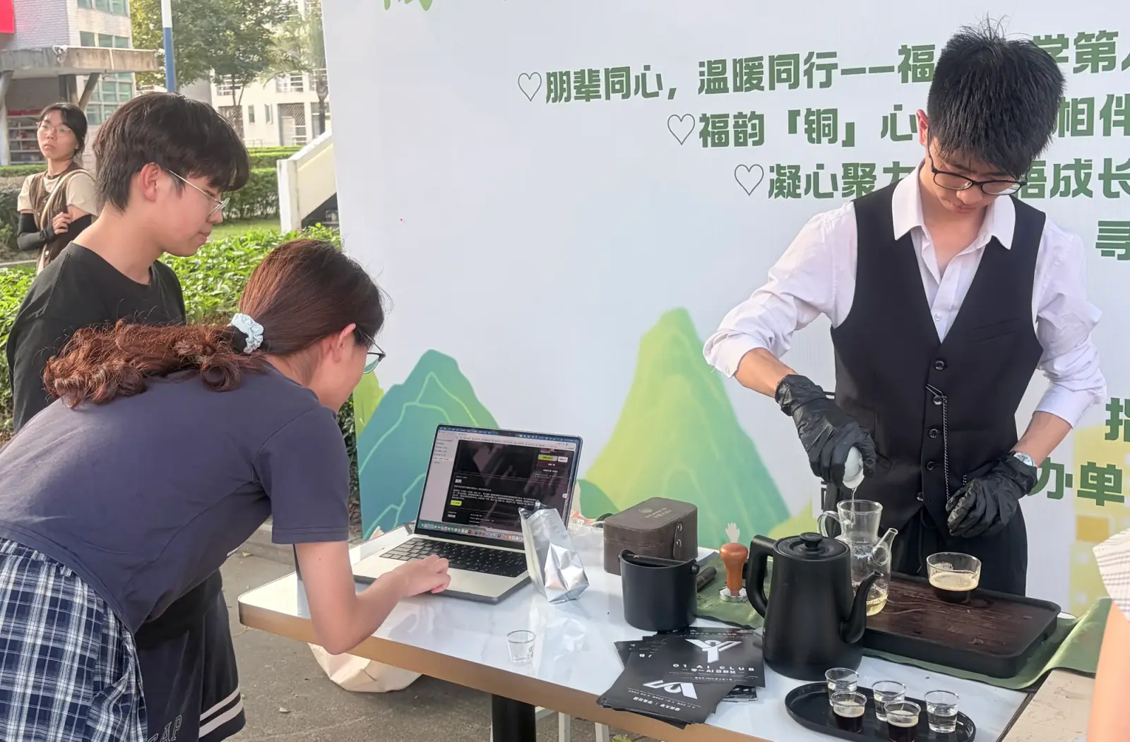 同学在电脑旁交流，工作人员在旁分享茶饮